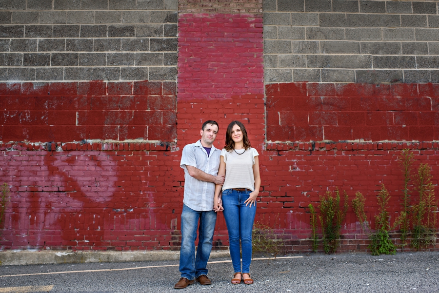 A hipster couple stand in front of a red and gray brick wall during their fishtown engagement session.